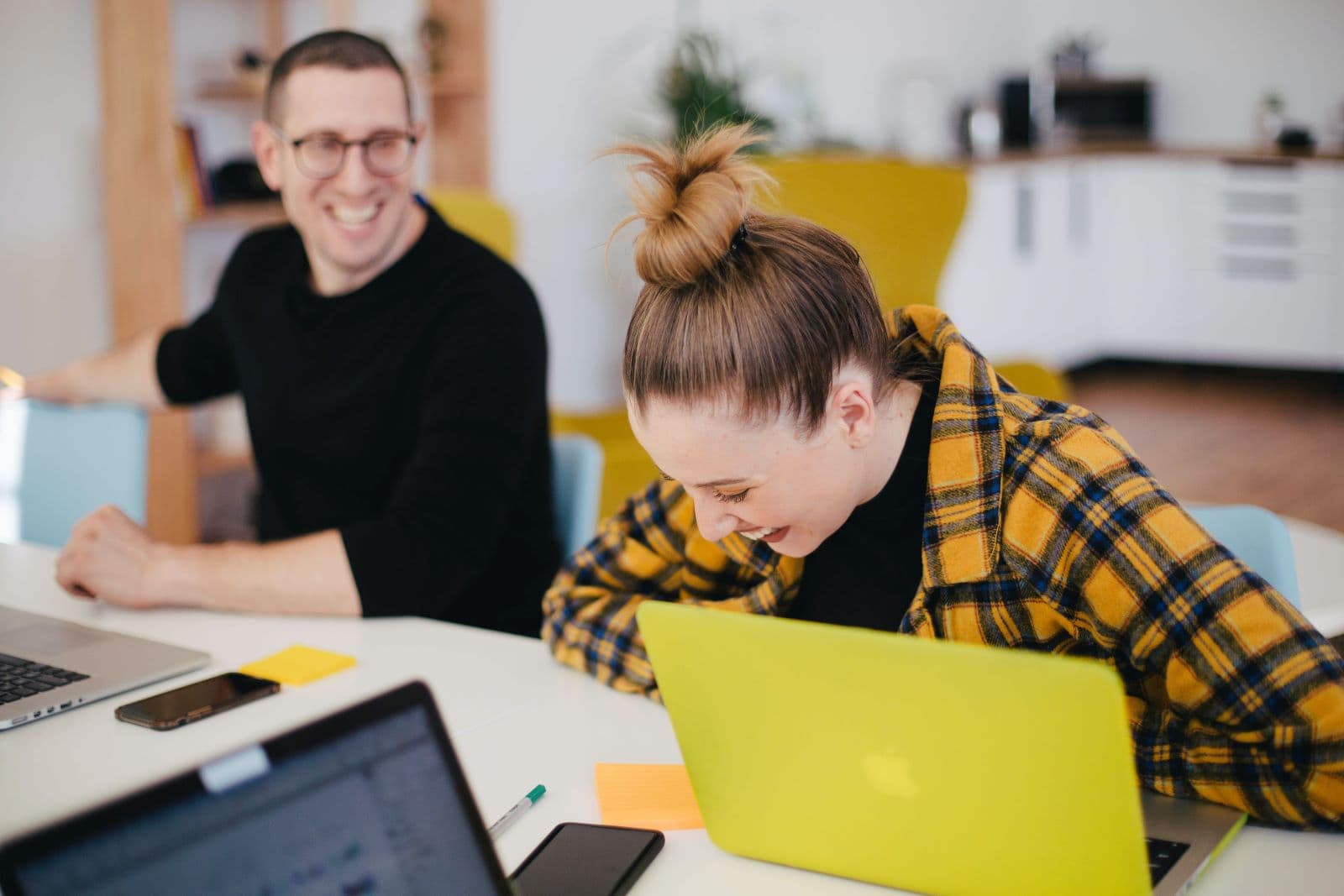 Man and woman laughing while working on laptops