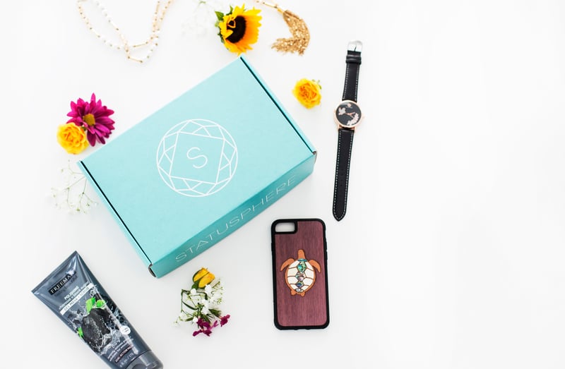 A Statusphere-branded box encircled by products including a skincare bottle, flowers, a watch and a phone