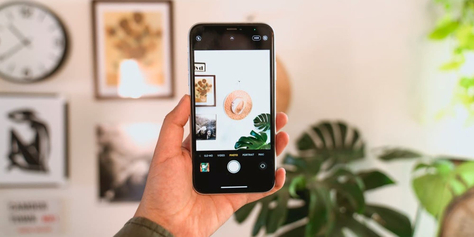 Hand raising a phone to photograph a hat hanging on the wall